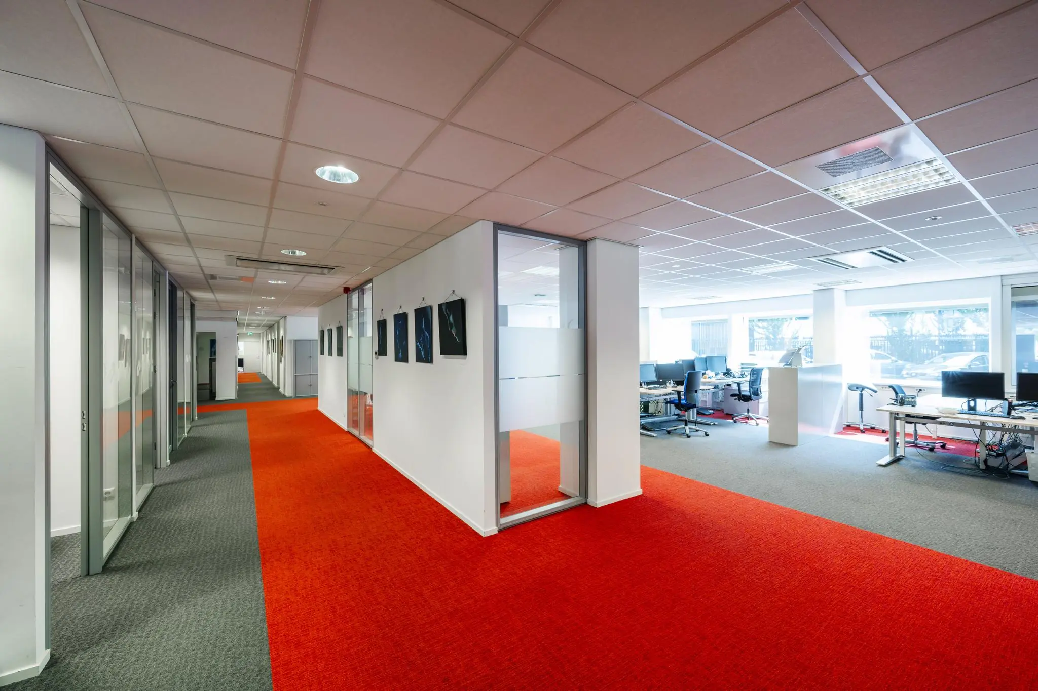 Moderne kantoorruimte aan de Jan Tooropstraat met open werkplekken, glazen wanden en rood-grijs tapijt.